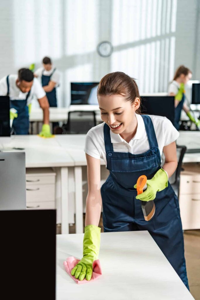 cheerful cleaner in overalls cleaning office desk with rag 1